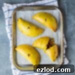 Irresistible Vegan Jamaican Veggie Patties 8 Four vegan Jamaican vegetable patties on a baking sheet on a blue and white tea towel.