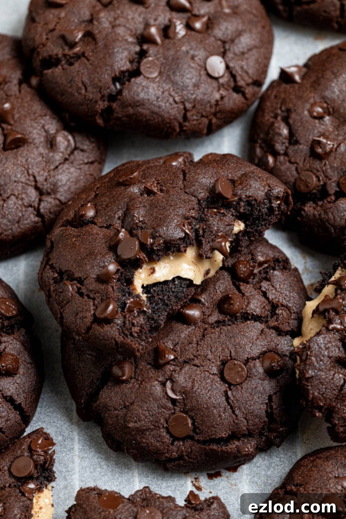 A beautiful pile of vegan peanut butter stuffed chocolate cookies, with one cookie expertly broken in half to reveal its luscious filling.