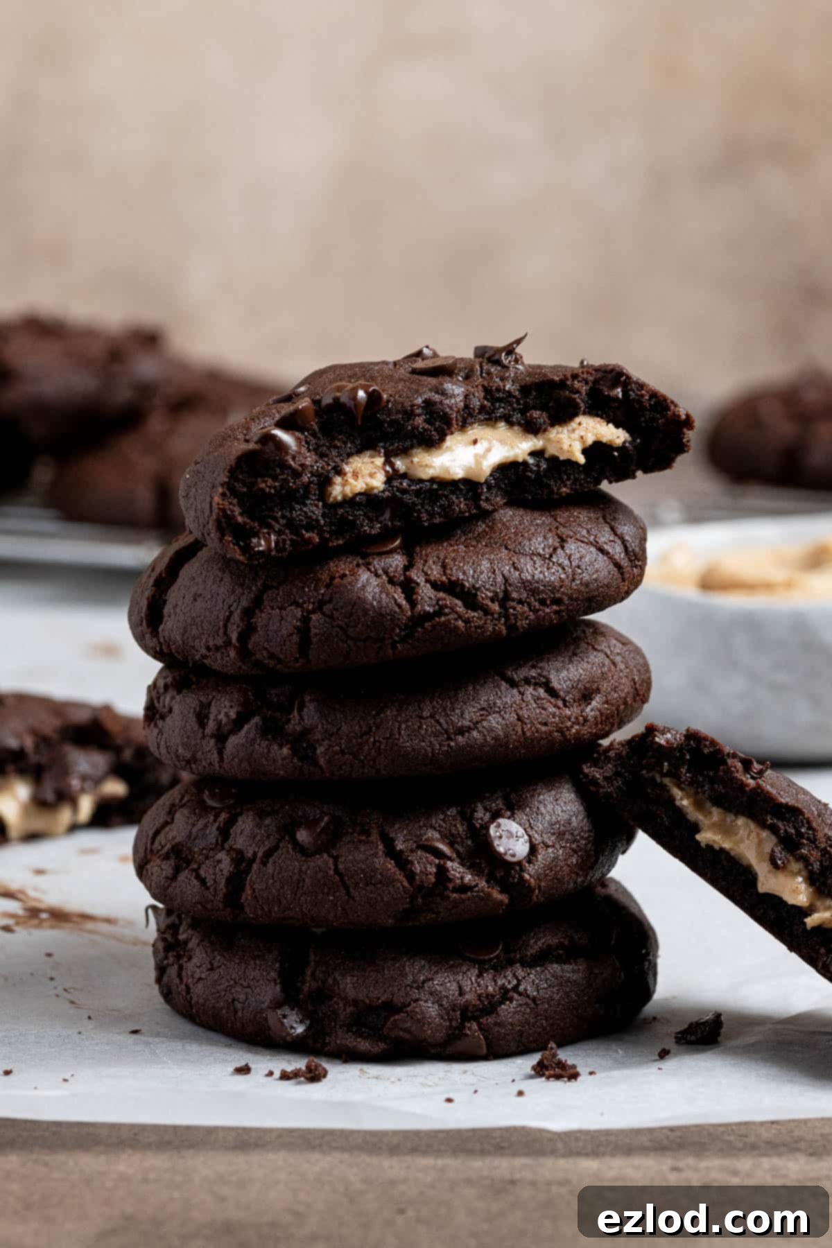 A stack of golden-brown vegan peanut butter stuffed chocolate cookies, with the top cookie broken to showcase its creamy center.