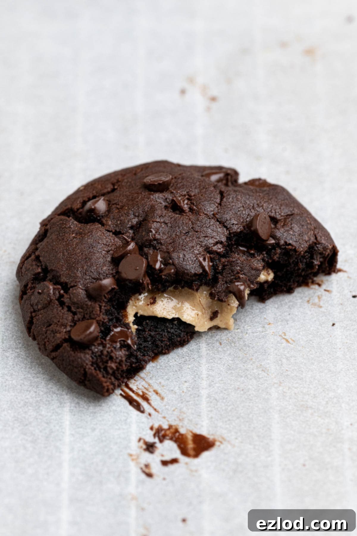 Close-up of a vegan peanut butter stuffed chocolate cookie with a piece broken off, showcasing the rich chocolate and creamy peanut butter.