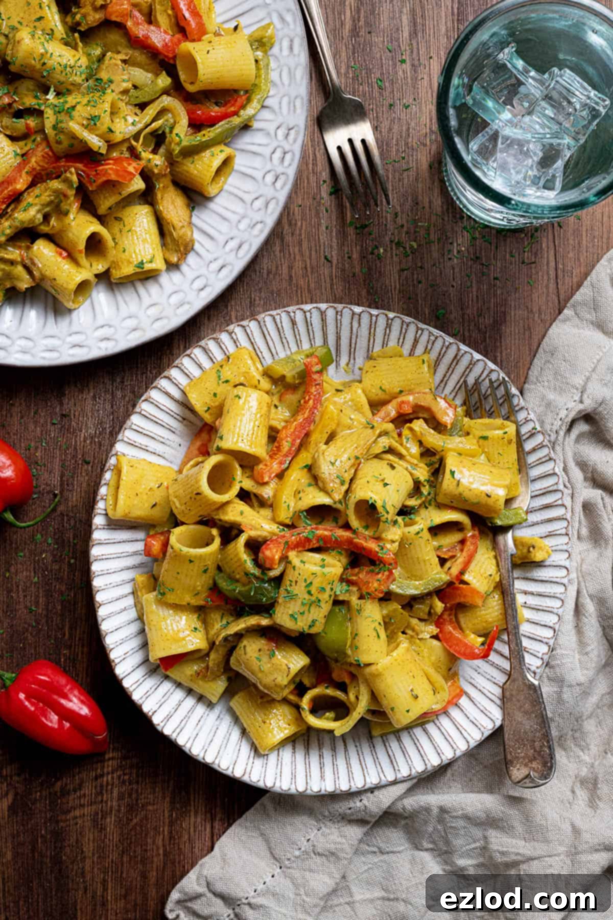 Two plates of vegan rasta pasta on a wooden surface with a glass of water.