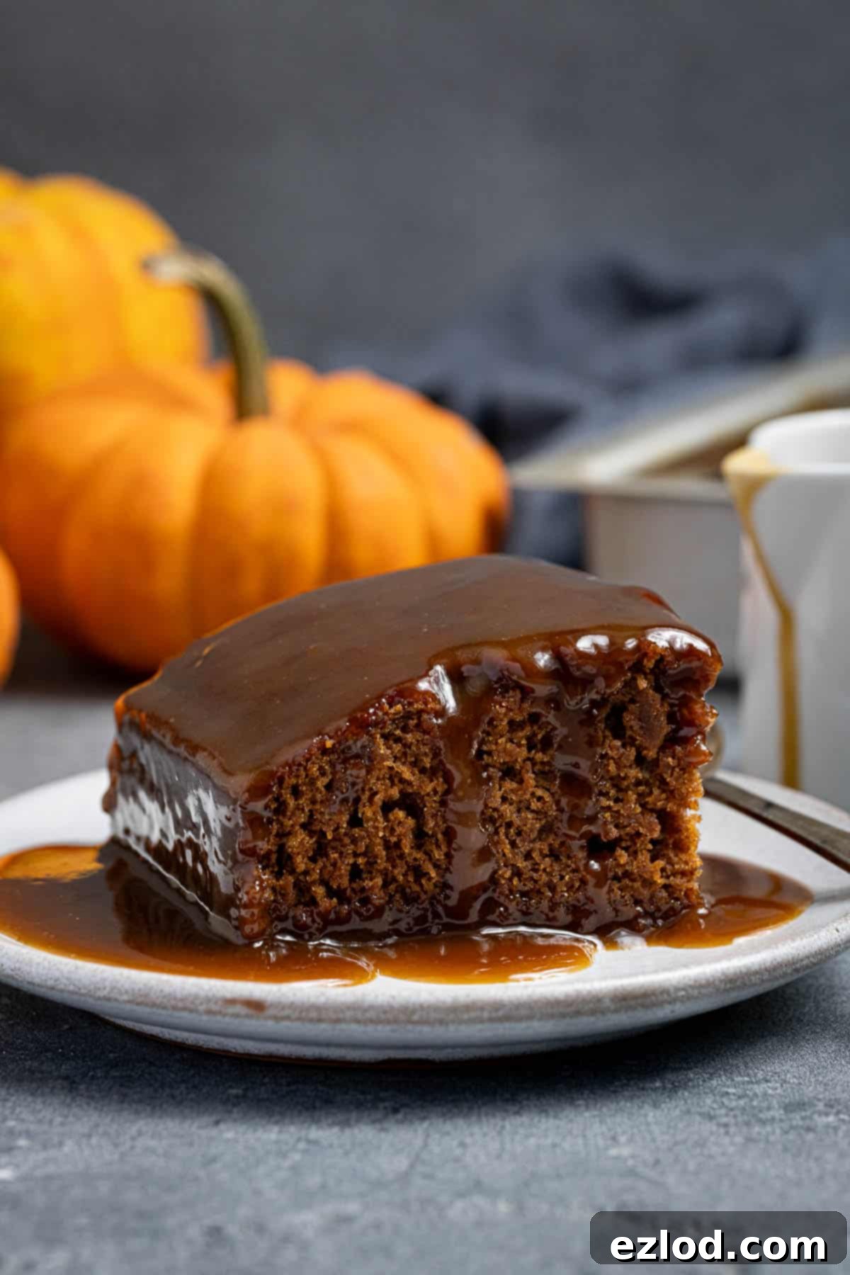 Spiced Pumpkin Sticky Toffee Pudding 14 A beautiful slice of vegan pumpkin sticky toffee pudding presented on a white plate, with charming mini pumpkins scattered in the soft-focus background, evoking an autumnal feel.