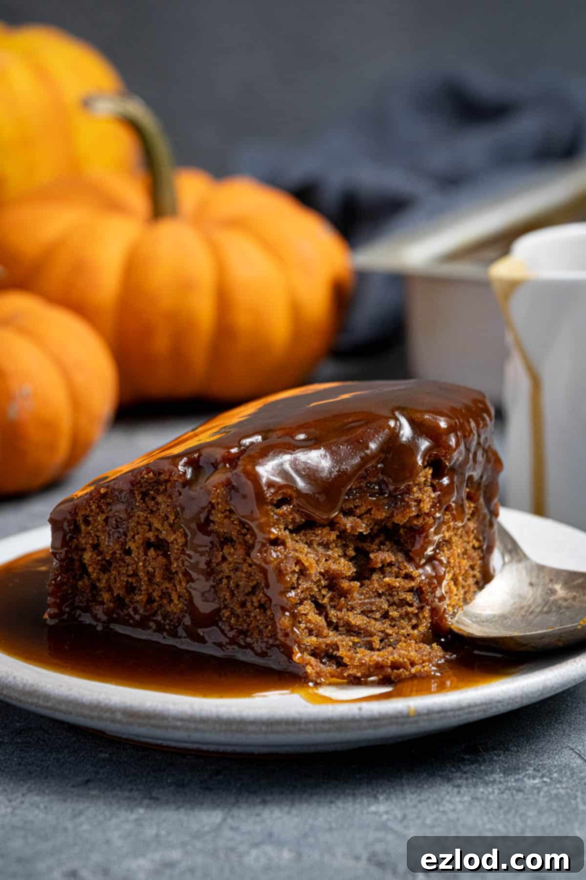 Spiced Pumpkin Sticky Toffee Pudding 4 A beautifully presented square of vegan pumpkin sticky toffee pudding on a white plate, with a spoonful delicately removed to show its moist interior. The background is softly blurred.