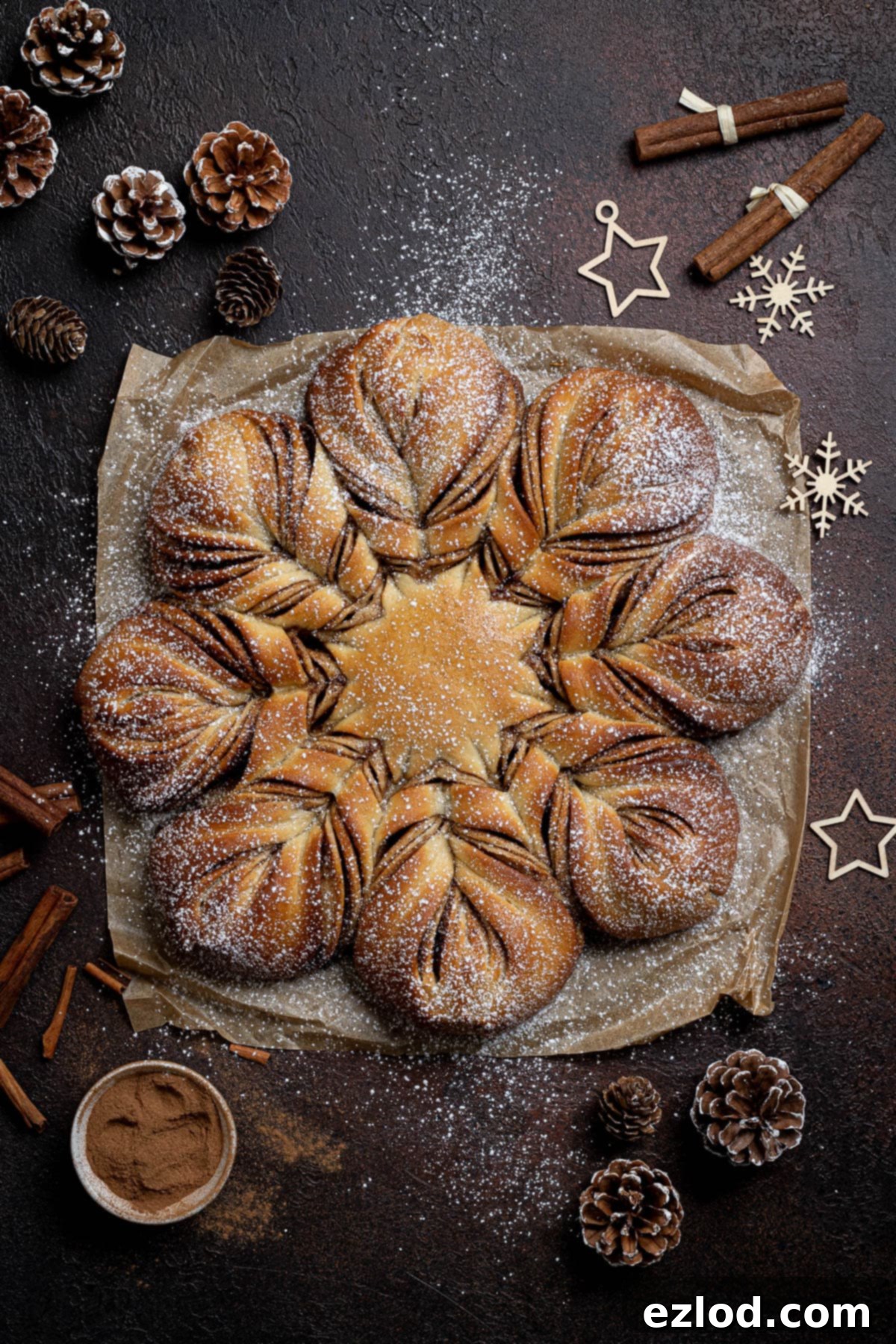 Vegan Cinnamon Star Bread 2 Vegan cinnamon star bread on a dark surface surrounded by cinnamon sticks, pine cones and Christmas decorations.