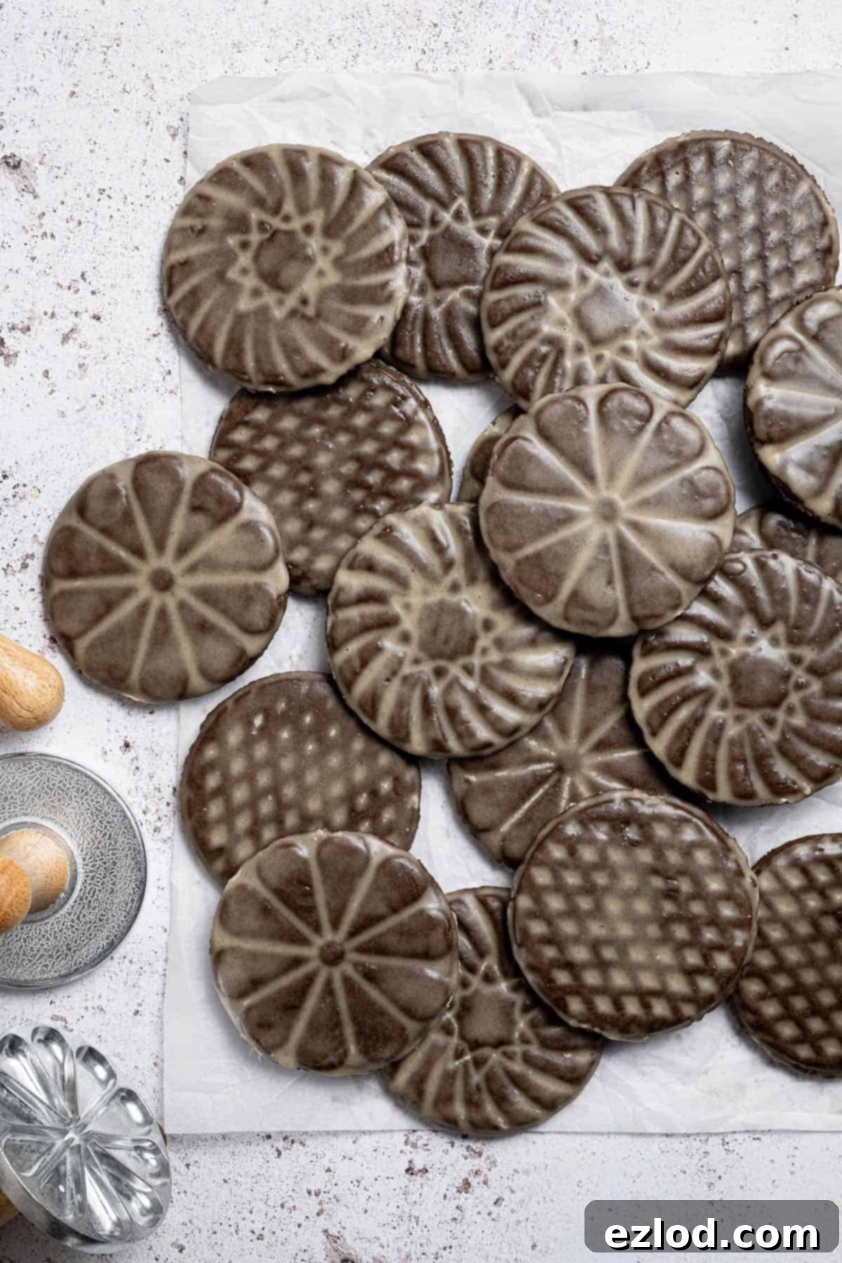 A tempting pile of vegan glazed gingerbread cookies on baking paper, accompanied by decorative metal cookie stamps.