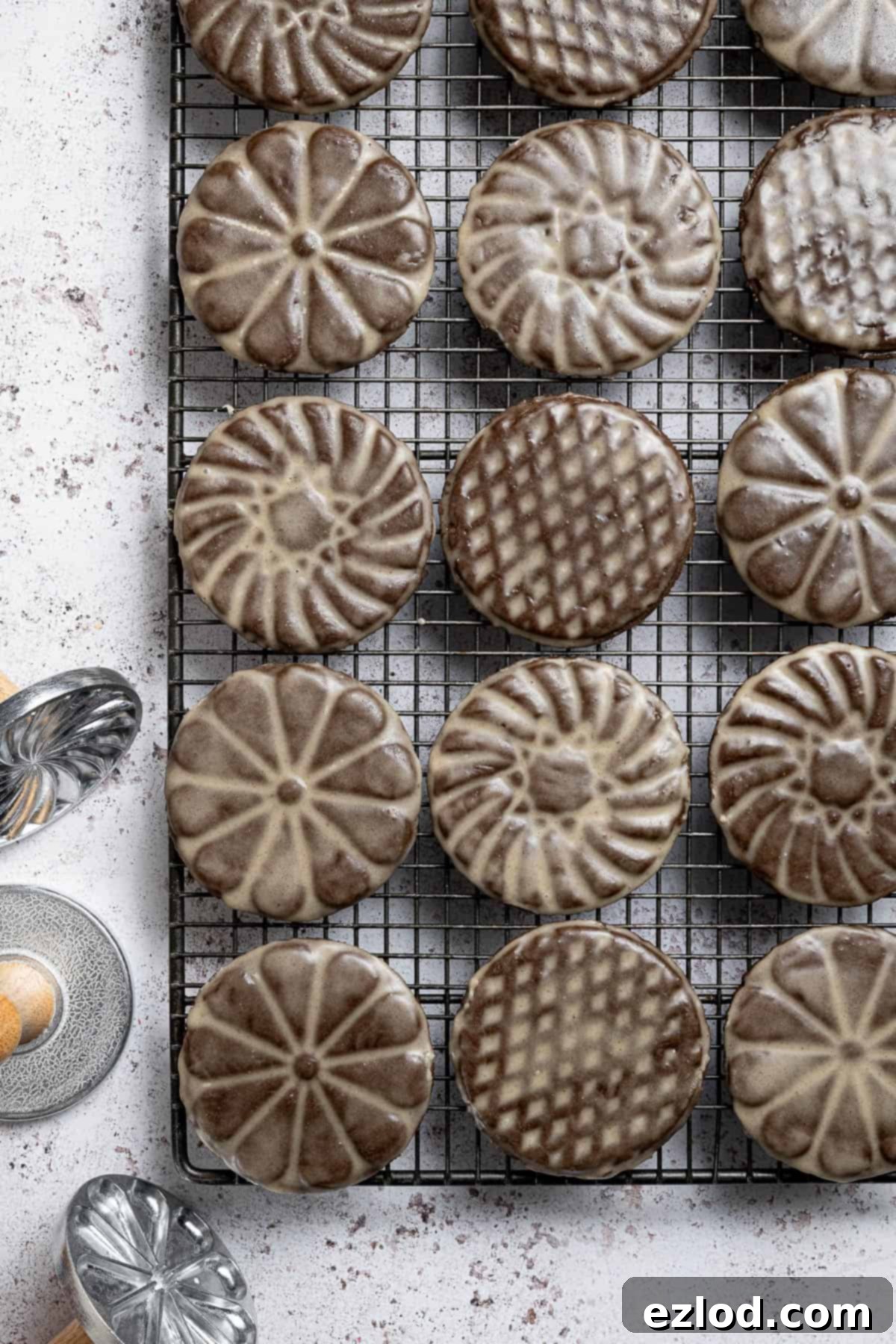 A batch of vegan glazed gingerbread cookies cooling on a wire rack, accompanied by decorative metal cookie stamps.