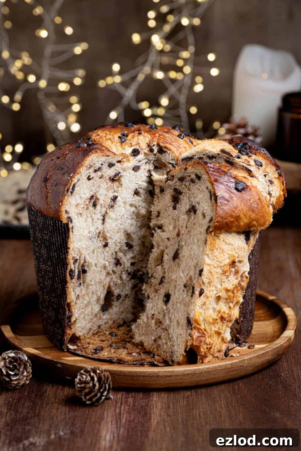 Slice vegan chocolate chip panettone on a wooden plate with Christmas lights and candles in the background.