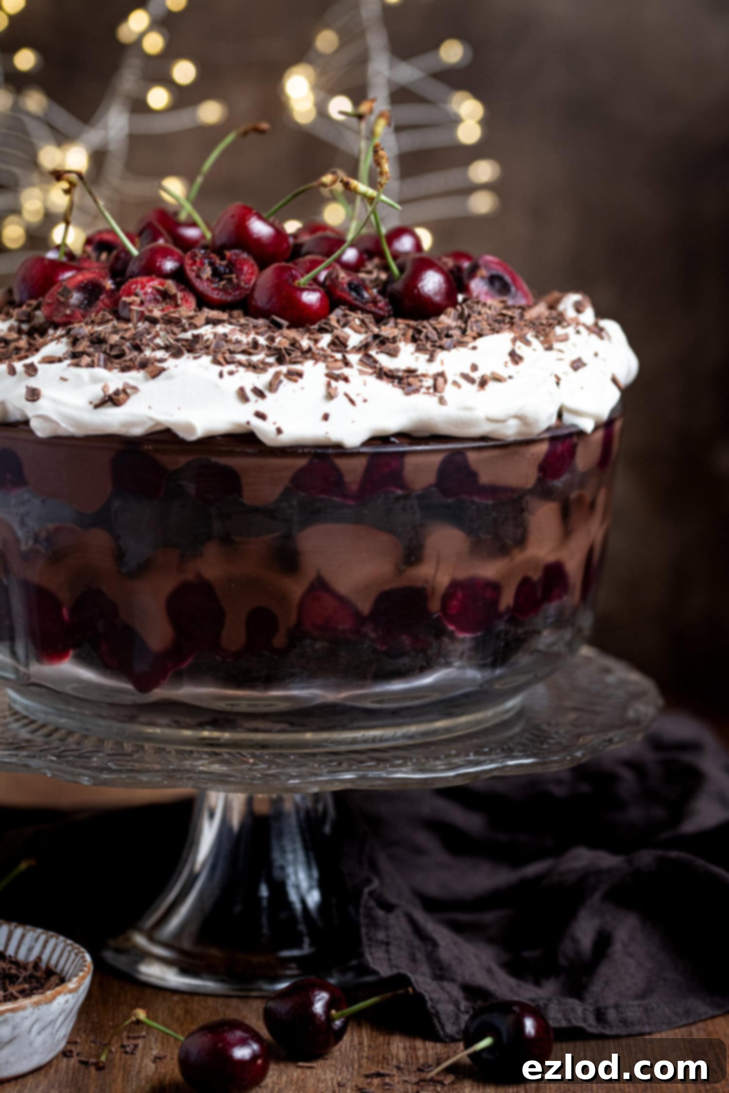 Vegan Dark Cherry Dream Trifle 13 Vegan black forest trifle topped with fresh cherries and chocolate shavings, on a glass cake stand.