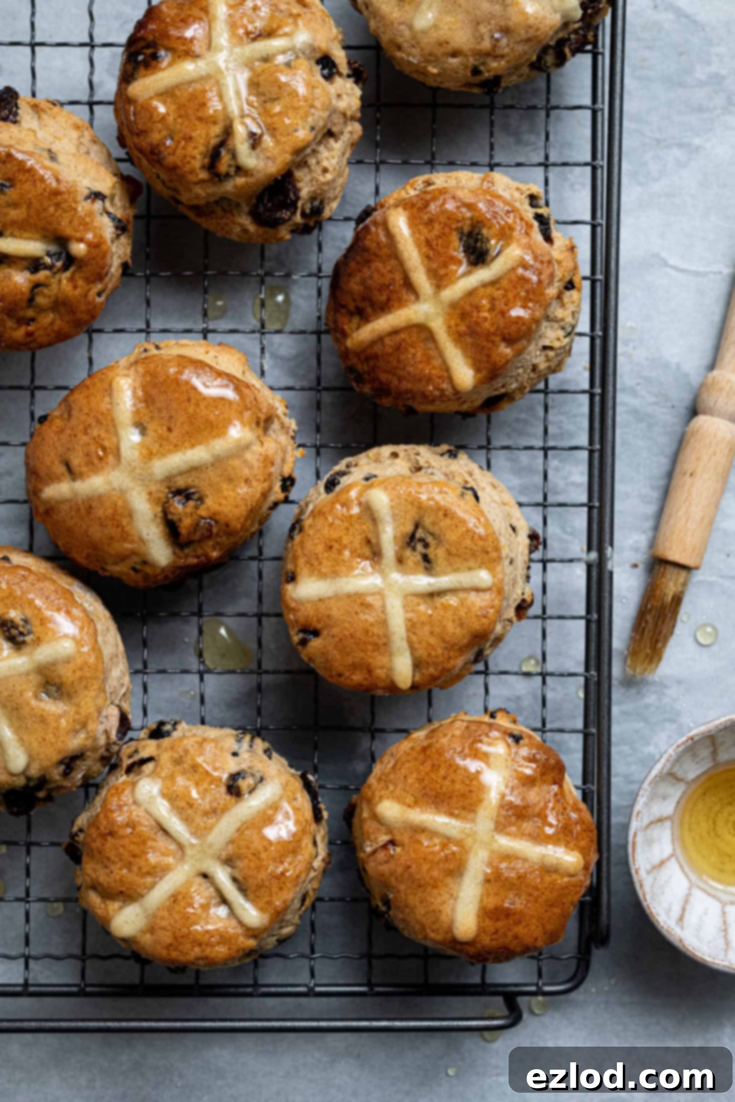 Vegan hot cross scones on a wire cooling rack with a bowl of syrup and a pastry brush.